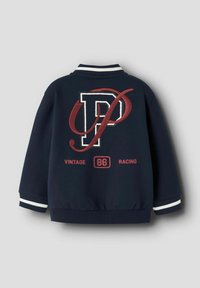 Granatowa kurtka z białymi paskami przy mankietach, z dużym haftowanym logiem "DP" w kolorze burgundowym oraz napisem "VINTAGE 86 RACING" na plecach.