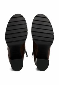 Bottes chelsea en cuir marron avec des semelles en caoutchouc noir texturé, dotées d'une fermeture éclair de chaque côté et d'un design à bout rond.