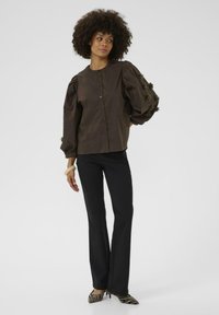 Brown, button-up shirt with puffed sleeves and textured accents, paired with black flared pants and striped pointed-toe shoes.