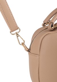 Sac à main en cuir beige avec une finition texturée, accessoires en or et une bandoulière amovible avec un fermoir en forme de homard. Détail zippé visible.