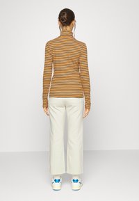 Camiseta de manga larga y cuello alto en rayas horizontales naranja y negro, combinada con pantalones de pierna ancha blancos y zapatillas con acentos azules.