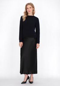 Navyblauwe gebreide trui met lange mouwen, gecombineerd met een zwarte satijnen maxirok en zwarte hoge hakken, wat een slanke silhouet creëert.