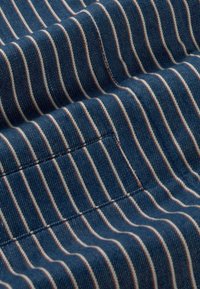 Detailný záber modrej látky s bielymi a červenými vertikálnymi pruhmi a viditeľným prešitím vytvárajúcim textúrované záhyby.