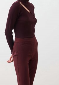 Burgundy ribbed turtleneck dengan detail potongan diagonal, dipadukan dengan celana high-waisted yang serasi dengan tekstur halus dan saku samping.