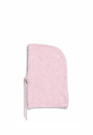 Mujer con un abrigo largo de pelo sintético gris, pantalones negros, zapatos negros y una gran capucha de punto rosa con cordones.