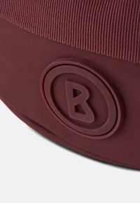 Prodotto rotondo bordeaux con superficie texturizzata, caratterizzato da un logo circolare prominente impresso in un colore coordinato.