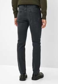 Jeans noirs ajustés en denim extensible, avec deux poches arrière, un léger délavage et une fermeture éclair. Portés avec des chaussures noires à semelle épaisse.