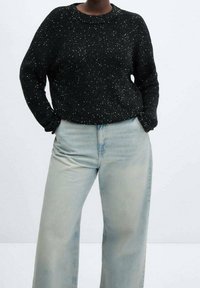 Czarny sweter dzianinowy z białymi cętkami, okrągłym dekoltem i długimi rękawami, w połączeniu z jasnoniebieskimi, szerokimi spodniami.