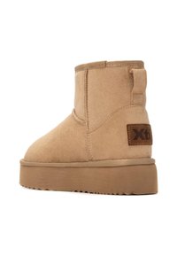 Botas de tobillo marrones de ante con suela plana, con un diseño cosido y un parche de cuero de marca marrón en el costado.