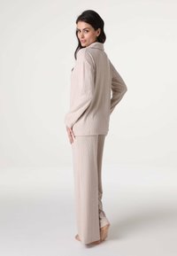 Completo pigiama beige a maglia con maniche lunghe e pantaloni dritti, caratterizzato da un motivo testurizzato e un materiale morbido.