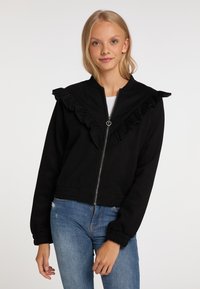Giacca nera con zip e dettagli del colletto arricciato. Maniche lunghe, polsini aderenti e design accorciato. Abbinata a jeans in denim blu.