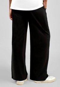 Pantaloni neri a gamba larga realizzati in tessuto liscio, con vita elastica e tasche laterali, abbinati a sneakers bianche.