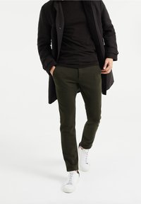 Olive green textured pants with a slim fit, paired with a black long coat and white sneakers. The fabric features a raised pattern.