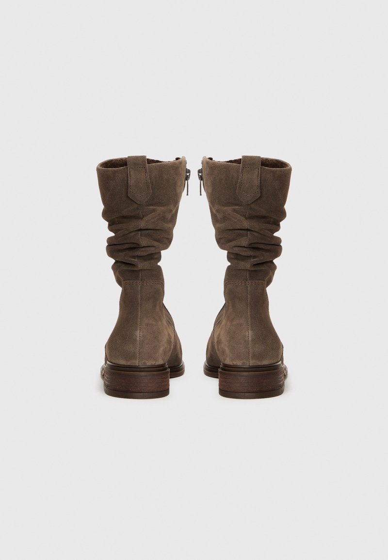 Botas de ante marrón hasta la mitad de la pantorrilla con un diseño holgado. Presentan un cierre lateral con cremallera, un tacón de madera plano y un puño enrollado para añadir textura y detalle.