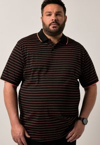 Camisa polo negra con rayas rojas horizontales, de mangas cortas, con cuello negro y tapeta de tres botones. Un acento notable es el contraste del cuello.