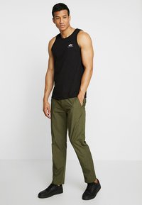 Svart ermeløs tanktop kombinert med olivengrønne tapered bukser og svarte joggesko. Tanktoppen har en liten merke-logo på brystet.