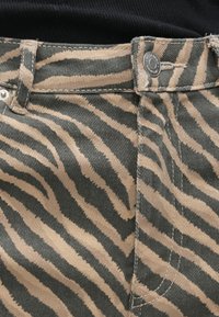 Nohavice so zebrovým vzorom v béžovej a tmavosivej farbe z manšestru, s predným zapínaním na gombíky a prešívanými detailmi pozdĺž švov.