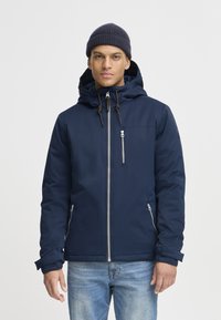 Navy winter jacket with a zip-up front, drawstring hood, side pockets, and ribbed cuffs. Smooth, insulated fabric with subtle texture.
