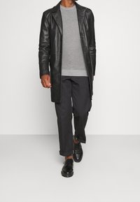 Sort læderjakke, gråstribet sweater, mørke bukser og sorte sko. Jakken har en klassisk pasform og knapdetaljer.