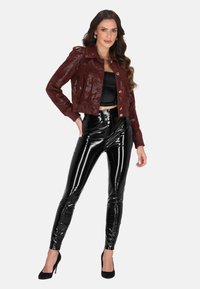 Burgundská lakovaná křiváková bunda s knoflíkovým zapínáním, doplněná o černé lesklé legíny s vysokým pasem. Černé vysoké podpatky dotvářejí celkový vzhled.