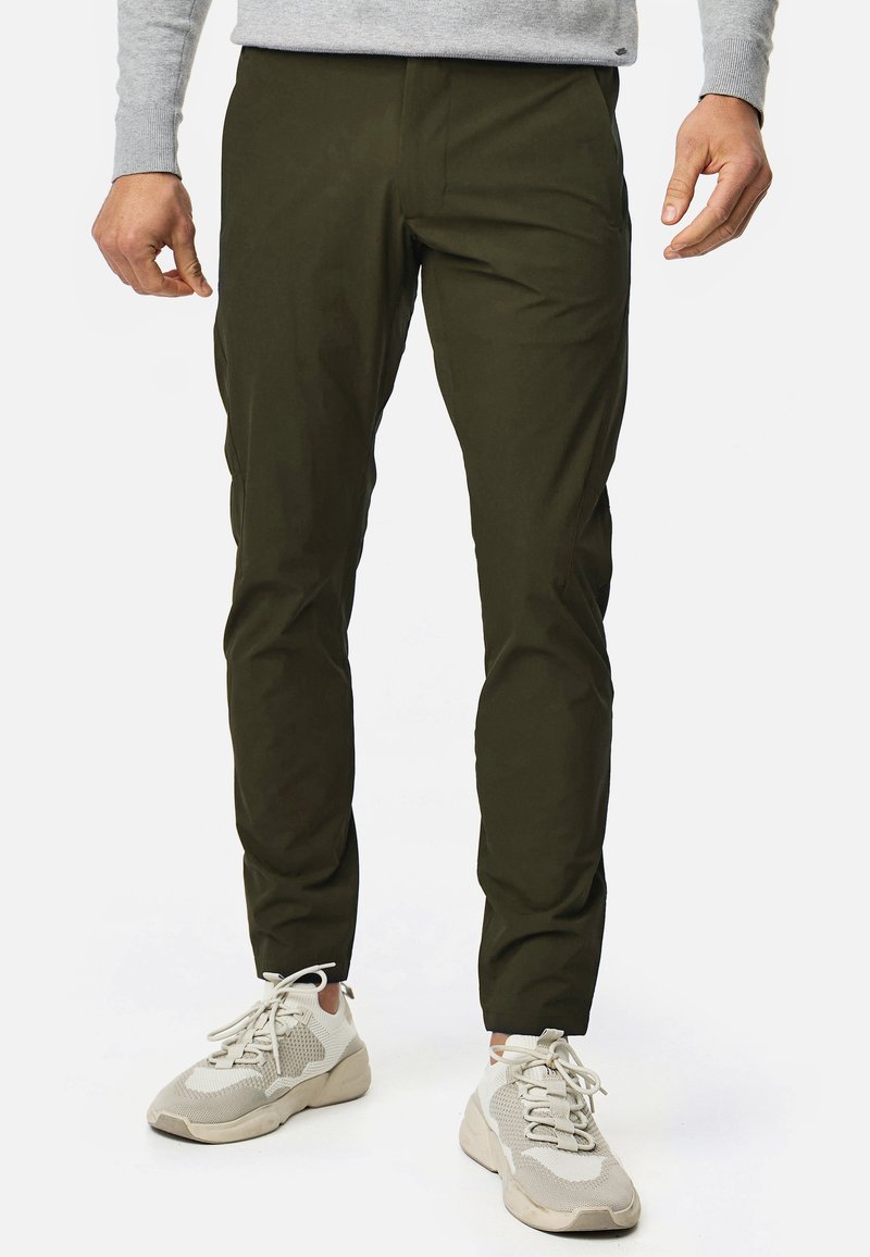 Olive green, slim-fit pants made from a lightweight material, featuring a smooth texture and minimal detailing. Paired with light gray sneakers.