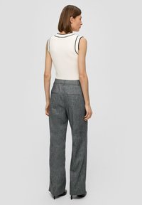 Haut sans manches blanc avec bord noir associé à un pantalon taille haute rayé gris. L'ensemble présente une coupe ajustée et un design minimaliste.