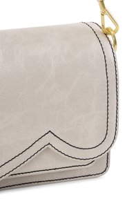 Lys beige fake lædertaske med en flap, der har sort syning og en buet detalje. Guld hardware til remmens vedhæftning.