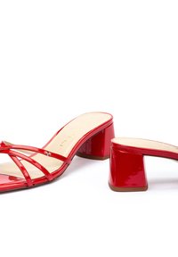 Des sandales à talons en cuir verni rouge présentent des lanières croisées et un talon carré. Texture lisse avec une semelle intérieure rembourrée et un discret logo.