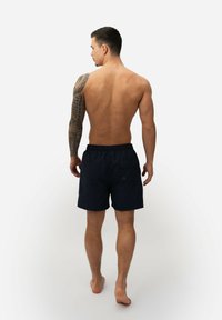 Marine zwemshorts met elastische taille, achterzak en kleine oogjes. Heeft een gladde stoftextuur en is boven de knie.