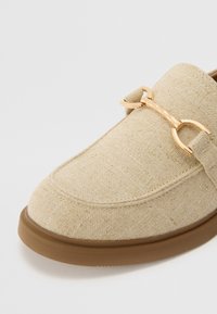 Beige szövet loaferek texturált kivitelben, barna gumitalppal. Az upper részen aranyszínű díszcsatt található.