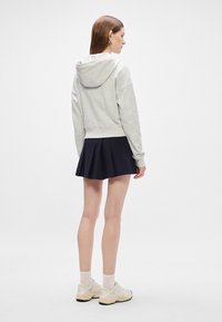 Γκρι hoodie με μπροστινή τσέπη και προσαρτημένη κουκούλα, σε συνδυασμό με μια σκούρα μπλε πλισέ φούστα. Τα υποδήματα περιλαμβάνουν ανοιχτόχρωμα αθλητικά παπούτσια.