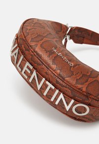 Punainen käärmekuvioinen laukku pyöreällä muotoilulla. Hopeinen "VALENTINO"-logoyksityiskohta ja teksturoitu pinta korostavat sen erottuvaa ulkonäköä.