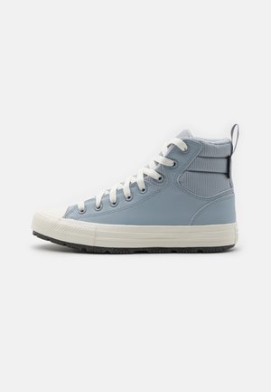 Zapatilla alta azul claro con cordones blancos, un cuello acolchado acanalado y una suela gruesa de goma blanca con una banda de rodadura negra.