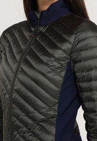 Lättviktsisolerad jacka i mörkgrön med kviltad textur. Har dragkedjestängning och kontrasterande sidopaneler i marinblå.