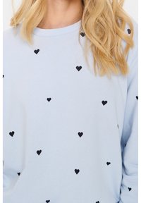 Felpa azzurra chiara in cotone, con piccoli motivi a cuore neri sparsi. Collo a giro classico e polsini a coste.