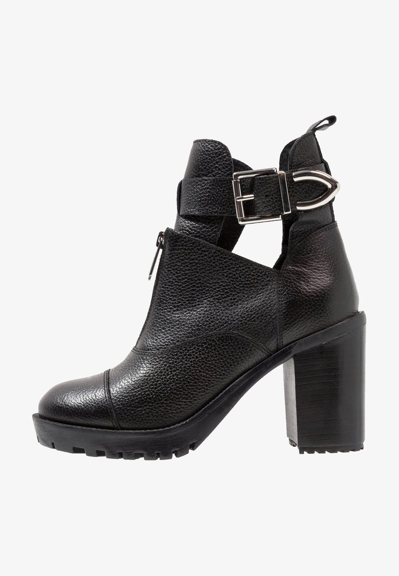 Bottine en cuir noir avec talon haut épais, fermeture éclair latérale et bride décorative à boucle argentée autour de la cheville.