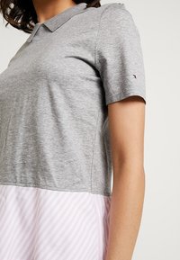 Top grigio in stile polo con maniche corte, abbinato a una gonna a righe rosa e bianche. Il materiale appare morbido e con una texture liscia. I dettagli includono un piccolo logo sulla manica.
