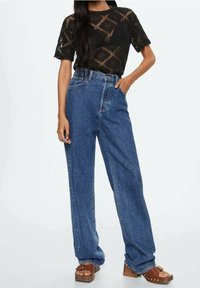 Black lace short-sleeve top with diamond pattern, paired with high-waisted, loose-fitting blue denim jeans and brown heeled sandals.