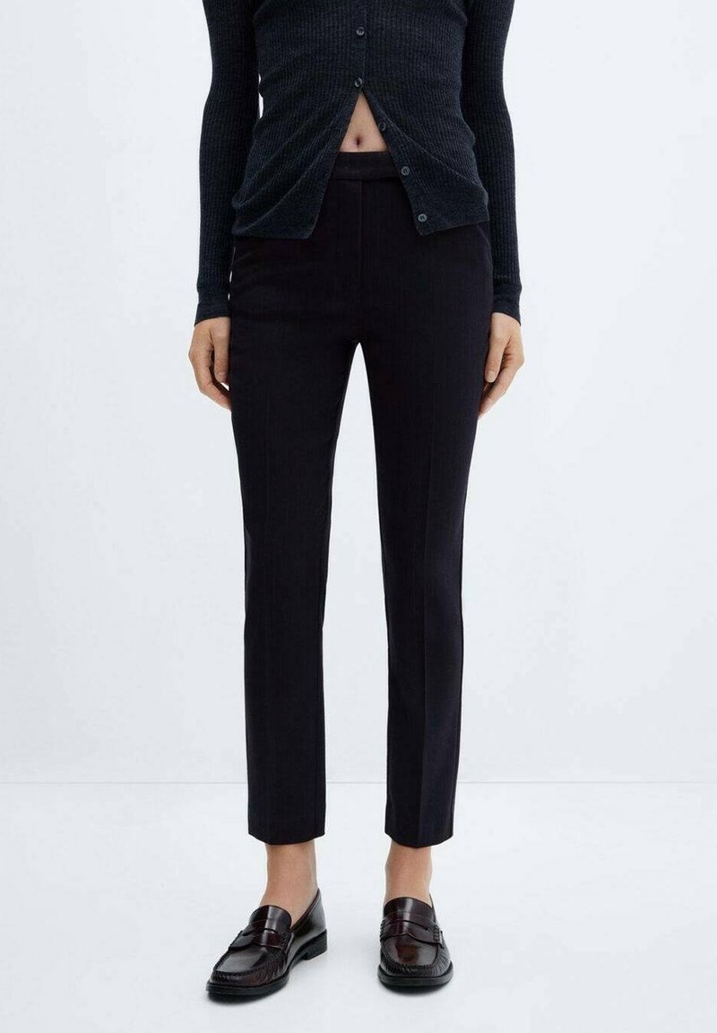 Pantalons ajustés sombres avec une coupe slim, présentant une texture lisse et de subtils rayures, associés à des mocassins brillants.
