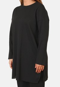 Tunic nera a coste con maniche lunghe, scollo rotondo, tessuto testurizzato, fessure laterali all'orlo e una vestibilità comoda.