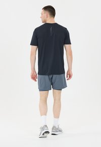 Marineblå kortærmet træningsshirt med diskret design på ryggen, parret med lysegrå shorts. Modellen har grå sneakers og hvide sokker på.