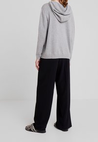 Sweatshirt à capuche gris, en tissu tricoté doux, coupe décontractée. Associé à un pantalon large noir et des sandales à rayures.