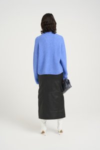 Blue knit sweater with oversized fit, black leather midi skirt, white heeled boots, and a black clutch purse. Minimalist design, textured fabric.
