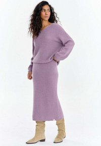 Fioletowy sweter dziany i pasująca do niego midi spódnica wykonane z miękkiego materiału. Strój cechuje się luźnym fasonem, długimi rękawami oraz bocznym akcentem w postaci metki.