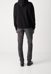 Sudadera con capucha negra de corte relajado y bolsillo tipo canguro, combinada con pantalones vaqueros grises de corte recto y textura sutil. Zapatos negros.