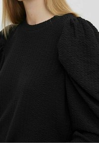Jersey negro texturizado con mangas abullonadas voluminosas y escote redondo, que presenta un patrón tejido para mayor profundidad y dimensión.