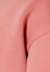 Närbild av ett rosa stickat tyg som visar fin struktur och en sömdetalj längs en böjd kant.