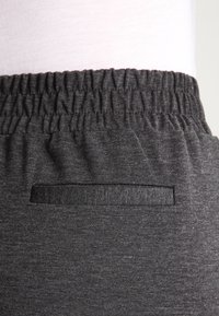 Pantaloni con elastico grigio in vita, realizzati in un tessuto liscio e texturizzato, con una piccola tasca laterale e un design minimalista.