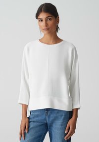 Witte geribbelde pullover met een ronde hals en driekwart mouwen. Heeft een rechte zoom en een gestructureerde afwerking, gecombineerd met blauwe jeans.