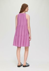 Ärmelloses rosa Schichtkleid mit gerafftem Ausschnitt und fließendem Rock. Kombiniert mit blauen Slippern mit strukturiertem Sohlen.